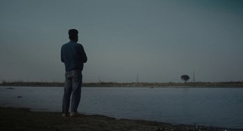 Movie still from “All That Breathes” (2022), directed by Shaunak Sen – A man standing on the shore of a body of water; Wide shot, Low angle
