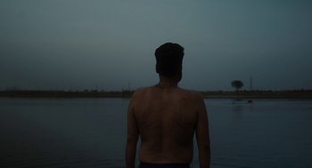 Movie still from “All That Breathes” (2022), directed by Shaunak Sen – A man standing in front of a body of water at night; Medium shot, Low angle