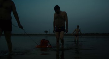 Movie still from “All That Breathes” (2022), directed by Shaunak Sen – A man walking across a body of water at night; Wide shot, Low angle