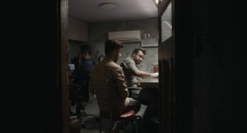 Movie still from “All That Breathes” (2022), directed by Shaunak Sen – A group of people sitting around a table; Wide shot, High angle