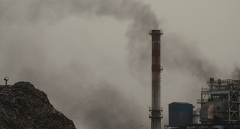 Movie still from “All That Breathes” (2022), directed by Shaunak Sen – Smoke billows out of a large industrial chimney; Extreme Wide shot, Low angle