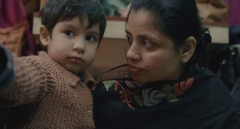 Movie still from “All That Breathes” (2022), directed by Shaunak Sen – A woman holding a child in her arms; Close Up shot, High angle