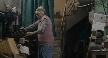 Movie still from “All That Breathes” (2022), directed by Shaunak Sen – An old man standing in front of a staircase; Wide shot, High angle