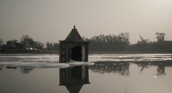 Movie still from “All That Breathes” (2022), directed by Shaunak Sen – A small building in the middle of a body of water; Extreme Wide shot, Low angle