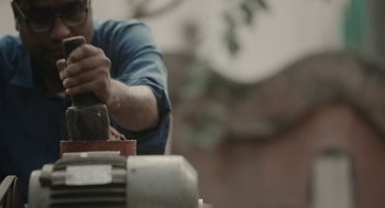Movie still from “All That Breathes” (2022), directed by Shaunak Sen – A man working on a piece of wood with a hammer; Medium shot, Low angle