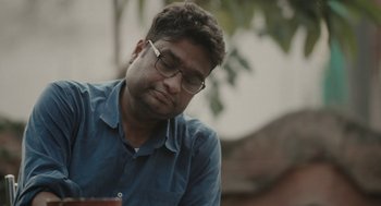 Movie still from “All That Breathes” (2022), directed by Shaunak Sen – A person wearing glasses and a blue shirt; Close Up shot, Low angle