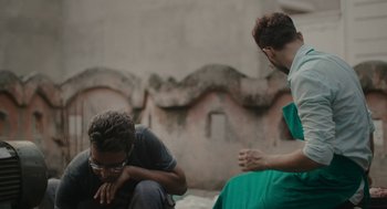 Movie still from “All That Breathes” (2022), directed by Shaunak Sen – Two men sitting on the side of a wall; Medium shot, Low angle