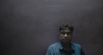 Movie still from “All That Breathes” (2022), directed by Shaunak Sen – A man in a blue shirt is standing in front of a gray wall; Close Up shot, Low angle
