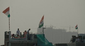 Movie still from “All That Breathes” (2022), directed by Shaunak Sen – People standing on a balcony with an indian flag flying; Extreme Wide shot, Low angle