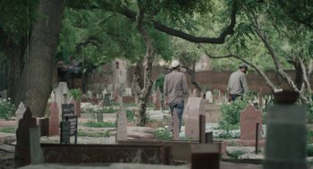 Movie still from “All That Breathes” (2022), directed by Shaunak Sen – Two men are standing in a cemetery near a tree; Wide shot, High angle