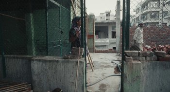 Movie still from “All That Breathes” (2022), directed by Shaunak Sen – A woman standing on a concrete wall in a building; Wide shot, High angle