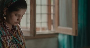 Movie still from “All That Breathes” (2022), directed by Shaunak Sen – A woman standing next to a window in front of a wall; Close Up shot, Over the shoulder angle