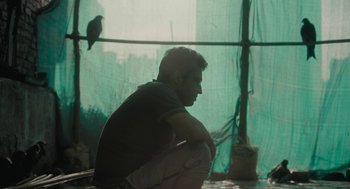 Movie still from “All That Breathes” (2022), directed by Shaunak Sen – A man sitting in front of a green tarpaulin; Medium shot, Low angle