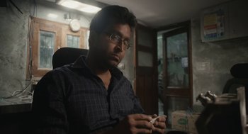 Movie still from “All That Breathes” (2022), directed by Shaunak Sen – A man sitting in a chair holding a cell phone; Close Up shot, Low angle