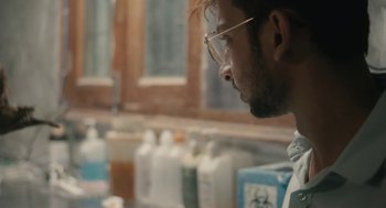 Movie still from “All That Breathes” (2022), directed by Shaunak Sen – A man wearing glasses looking at a window; Close Up shot, Over the shoulder angle