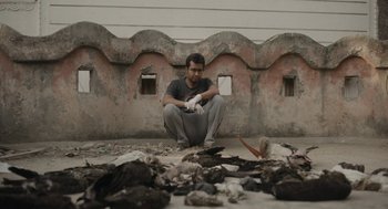 Movie still from “All That Breathes” (2022), directed by Shaunak Sen – A man kneeling on the ground looking at a pile of trash; Medium shot, Low angle