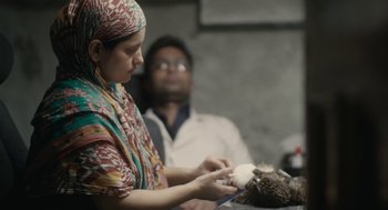 Movie still from “All That Breathes” (2022), directed by Shaunak Sen – A woman holding a cat while sitting next to a man; Close Up shot, Over the shoulder angle