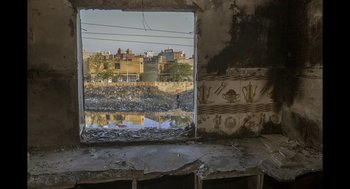 Movie still from “All That Breathes” (2022), directed by Shaunak Sen – A view of a city through a broken window; Extreme Wide shot, High angle