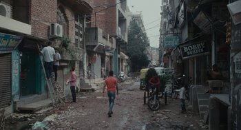Movie still from “All That Breathes” (2022), directed by Shaunak Sen – A group of people walking down a street near buildings; Wide shot, High angle