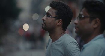 Movie still from “All That Breathes” (2022), directed by Shaunak Sen – A man with glasses is standing next to another man; Close Up shot, Low angle