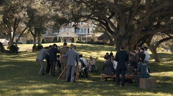 Movie still from “All the Way” (2016), directed by Jay Roach – A group of people gathered in the grass under a large tree; Extreme Wide shot, High angle
