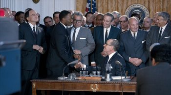 Movie still from “All the Way” (2016), directed by Jay Roach – A group of men standing around a man shaking his hand; Medium shot, Over the shoulder angle