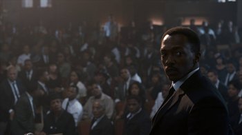 Movie still from “All the Way” (2016), directed by Jay Roach – A man in a suit standing in front of an audience; Medium shot, High angle