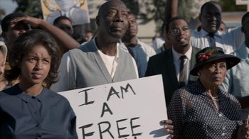 Movie still from “All the Way” (2016), directed by Jay Roach – A man holding a sign that says " i am a free man "; Medium shot, High angle