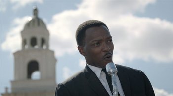 Movie still from “All the Way” (2016), directed by Jay Roach – A man wearing a suit and tie speaking into a microphone in front of a building; Close Up shot, Low angle