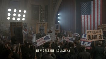 Movie still from “All the Way” (2016), directed by Jay Roach – A group of people holding up signs in front of an audience; Extreme Wide shot, High angle