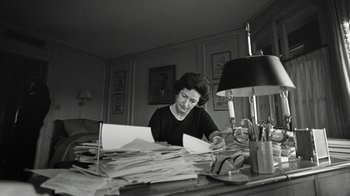 Movie still from “All the Way” (2016), directed by Jay Roach – A woman sitting at a desk with papers in front of a lamp; Medium shot, High angle