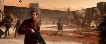 Movie still from “Allegiant” (2016), directed by Robert Schwentke – A young man holding a gun in front of a group of people; Wide shot, Over the shoulder angle