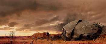 Movie still from “Allegiant” (2016), directed by Robert Schwentke – Two people standing on a dirt field under a cloudy sky; Extreme Wide shot, Low angle