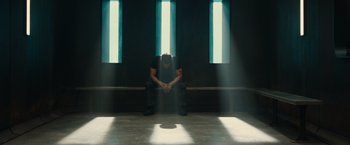 Movie still from “Allegiant” (2016), directed by Robert Schwentke – A man sitting on the ground in a room with light coming through the windows; Wide shot, Low angle