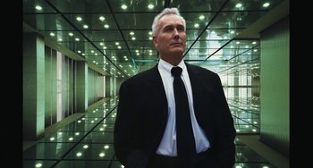 Movie still from “Aloha” (2015), directed by Cameron Crowe – A man in a suit and tie standing in a building; Medium shot, Low angle