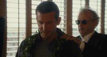 Movie still from “Aloha” (2015), directed by Cameron Crowe – A man with a lei around his neck is being hugged by another man; Close Up shot, Over the shoulder angle