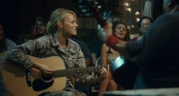Movie still from “Aloha” (2015), directed by Cameron Crowe – A woman is playing a guitar while others watch; Medium shot, Over the shoulder angle