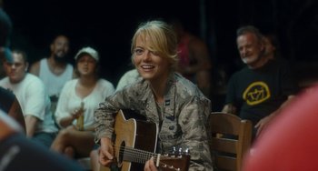 Movie still from “Aloha” (2015), directed by Cameron Crowe – A woman sitting in front of an acoustic guitar in front of a group of people; Medium shot, Over the shoulder angle