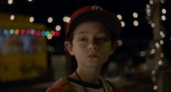 Movie still from “Aloha” (2015), directed by Cameron Crowe – A young boy wearing a baseball cap in the dark; Close Up shot, Over the shoulder angle