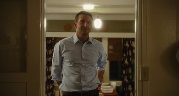 Movie still from “Aloha” (2015), directed by Cameron Crowe – A man standing in front of a mirror in a room; Medium shot, Over the shoulder angle