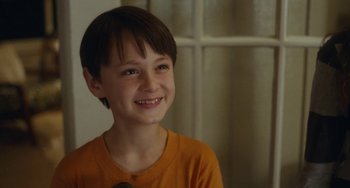 Movie still from “Aloha” (2015), directed by Cameron Crowe – A young boy smiling for the camera in front of a window; Close Up shot, Over the shoulder angle