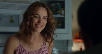 Movie still from “Aloha” (2015), directed by Cameron Crowe – A woman smiles brightly while sitting in front of a counter; Close Up shot, Over the shoulder angle