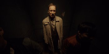 Movie still from “Fargo” (2014), created by Noah Hawley – A man in a trench coat standing in a dark room; Medium shot, Low angle