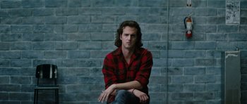 Movie still from “American Animals” (2018), directed by Bart Layton – A man sitting on the ground in front of a brick wall; Close Up shot, Low angle