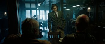 Movie still from “American Animals” (2018), directed by Bart Layton – A man in a suit and tie standing at a table; Medium shot, Low angle
