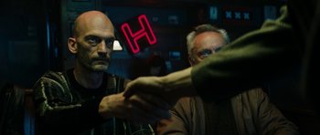 Movie still from “American Animals” (2018), directed by Bart Layton – Two men shaking hands in a bar with a neon sign in the background; Medium shot, Over the shoulder angle