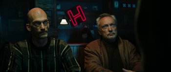 Movie still from “American Animals” (2018), directed by Bart Layton – An older man sitting at a table in front of a neon sign; Medium shot, Over the shoulder angle