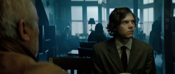 Movie still from “American Animals” (2018), directed by Bart Layton – A man in a suit sitting in front of a table; Medium shot, Over the shoulder angle