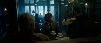 Movie still from “American Animals” (2018), directed by Bart Layton – A man sitting at a table in front of two other men; Medium shot, Over the shoulder angle