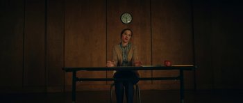 Movie still from “American Animals” (2018), directed by Bart Layton – A woman sitting at a table in front of a clock; Medium shot, Low angle